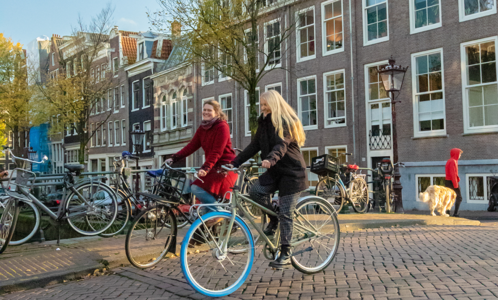 two smiling women on bikes in amsterdam